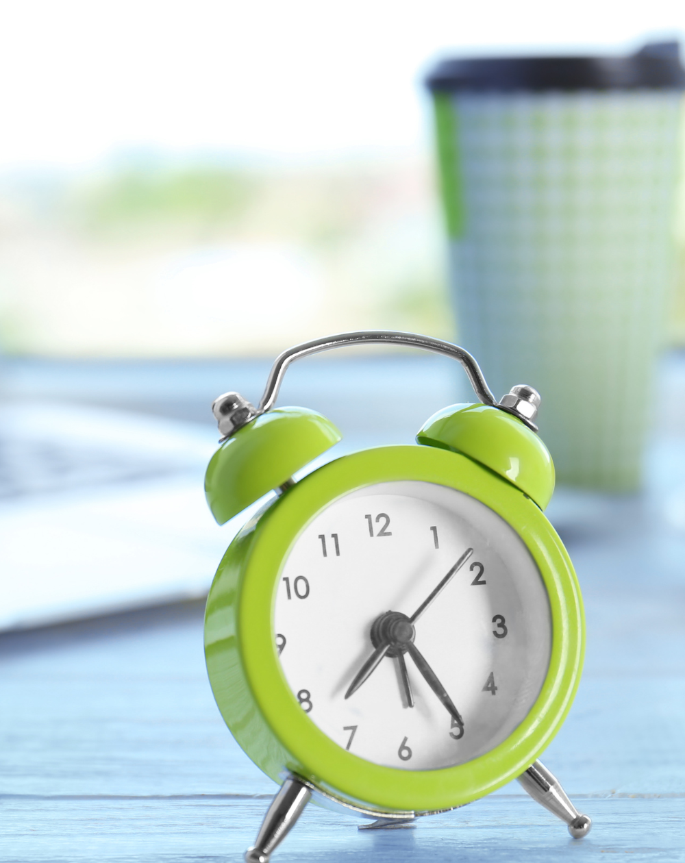 An illustrative image for a blog post about daily routines. In the foreground, a lime green alarm clock takes center stage on a well-kept desk, symbolizing the importance of time management in one's daily routine. In the background, a laptop, a delicious croissant, and a light blue disposable coffee cup hint at the elements that make up a morning ritual.